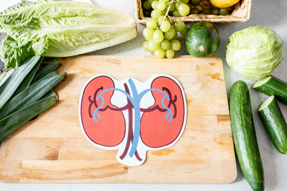 Kidney diagram surrounded by green vegetables and fruits that promote kidney function