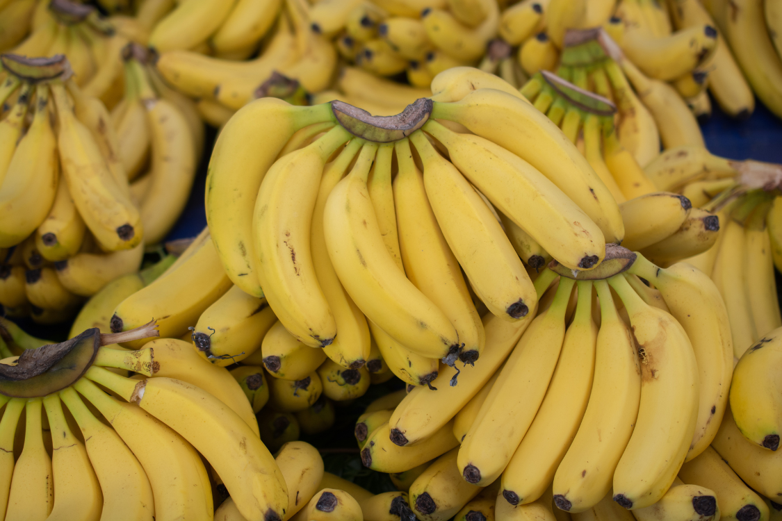 Multiple bunches of ripe yellow bananas displayed at a market, illustrating a safe, low-purine fruit choice for managing gout.