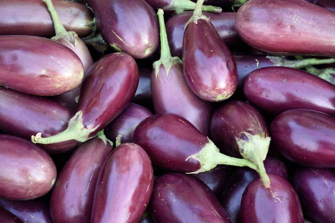 Close-up of a pile of raw, dark purple eggplants, a low-purine nightshade vegetable.
