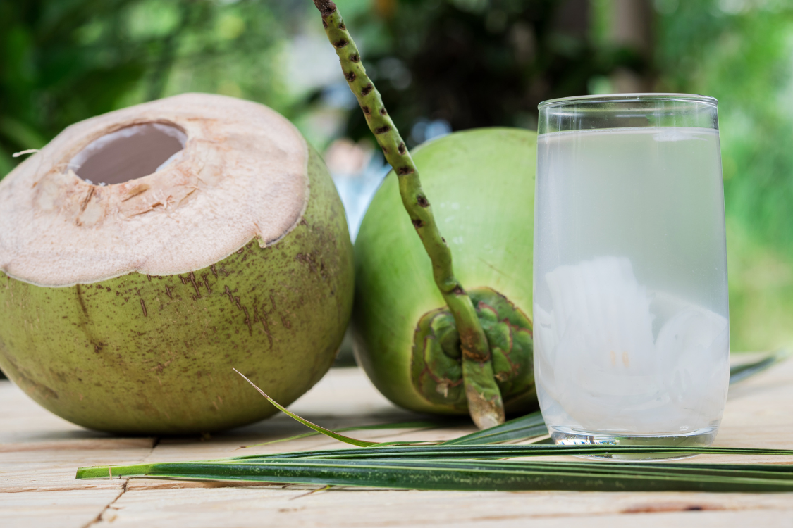 Fresh coconut water in a glass beside green coconuts, linked to kidney stone hydration benefits.