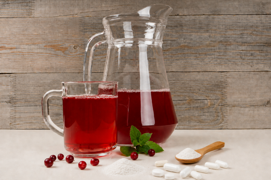 and lower concentration of active compounds may make it less suitable for kidney-focused urinary support. A glass pitcher and mug filled with red cranberry juice beside cranberries, mint, white powder, and capsules, representing the trade-offs of juice co