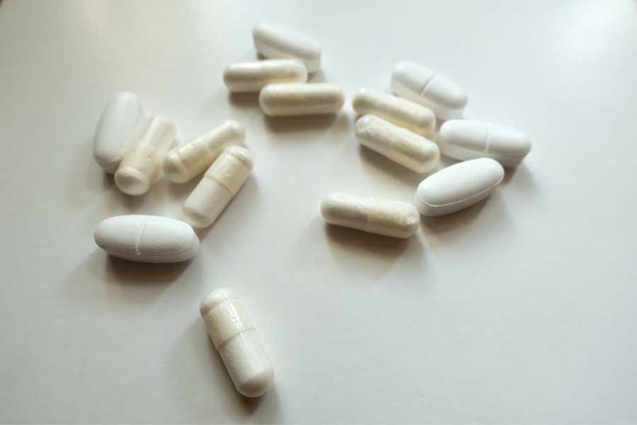 Scattered white tablets and capsules used to represent daily kidney stone medication and treatment adherence.