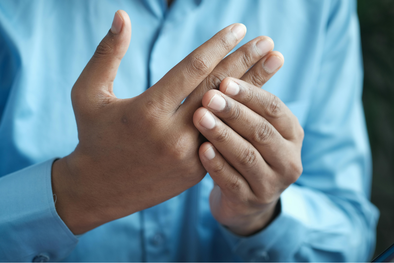 Close-up of hands massaging fingers for gout pain relief, person wearing light blue shirt
