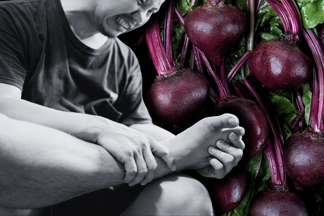 A man holding his painful foot next to a background of fresh beets, suggesting possible gout triggers.