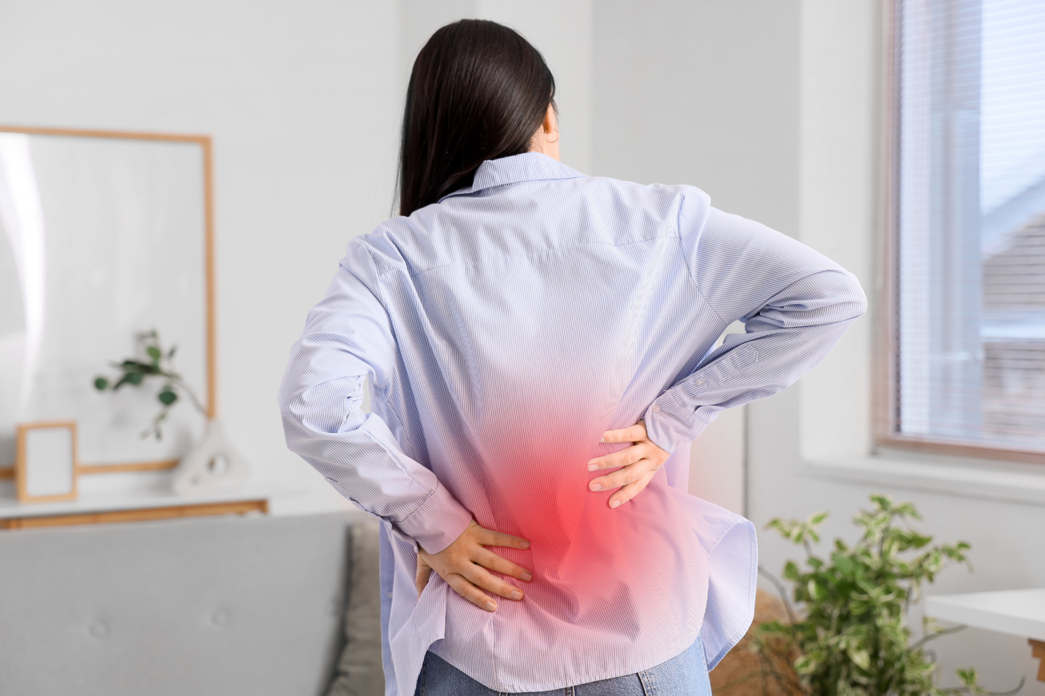 Woman holding her lower back while experiencing pain at home.