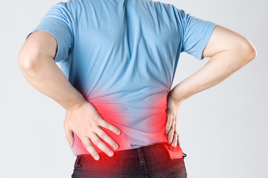 A man viewed from behind wearing a blue shirt, holding his lower back with both hands where a red glow indicates broad muscle pain.