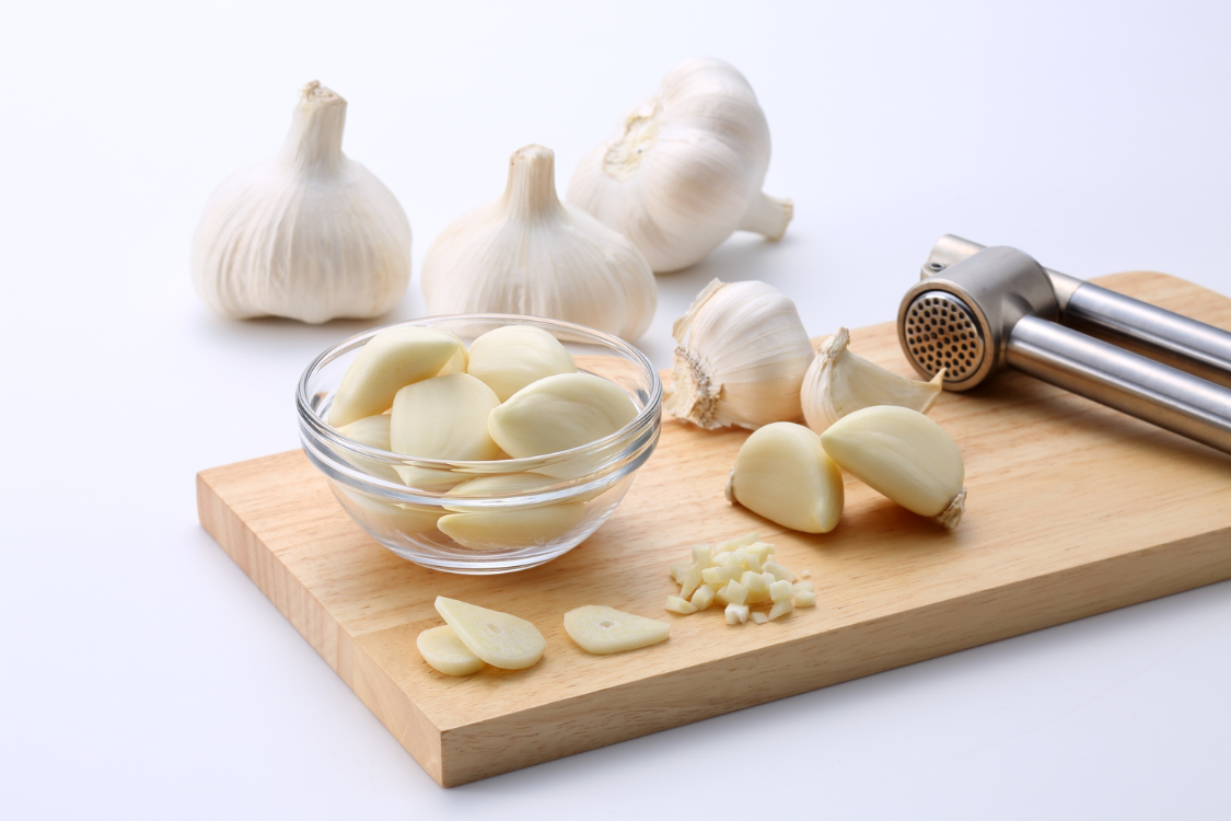 Peeled and chopped garlic cloves on a cutting board with a press, showing the preparation of fresh garlic for cooking, which is safer than supplements for kidney patients.