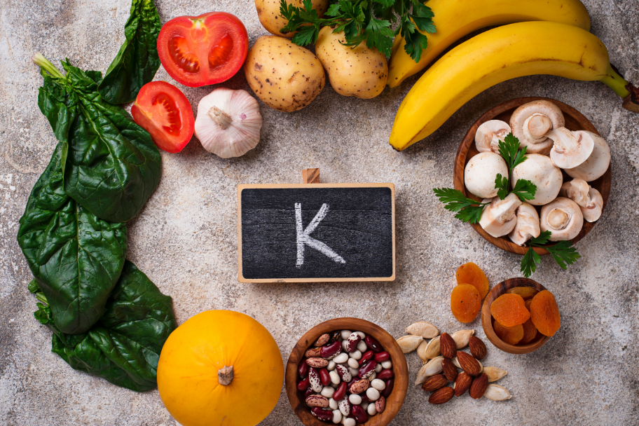 Fresh potassium-rich foods like bananas, spinach, beans, and tomatoes arranged around a chalkboard with the letter K