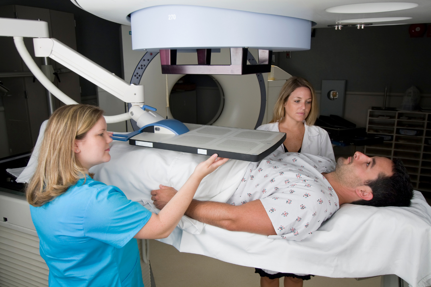 Two female medical professionals preparing a male patient on a table for an imaging scan, often done before prostate surgery.