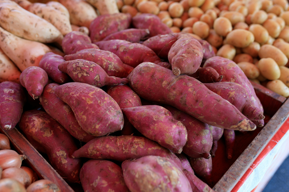 A pile of raw sweet potatoes in a market, a beneficial vegetable for gout sufferers, providing nutrients without increasing uric acid levels or contributing to purine metabolism issues.