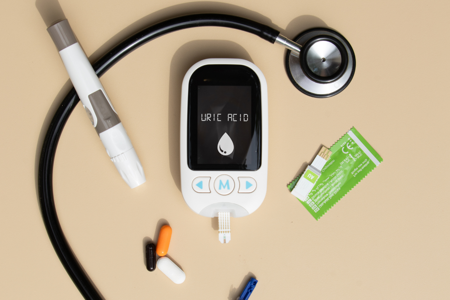A uric acid meter with a lancet, stethoscope, test strips, and pills arranged on a beige background.