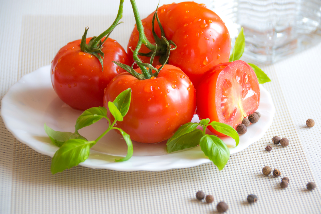 Whole and half-sliced red tomatoes on a white plate with fresh basil, emphasizing the importance of tomato for prostate health in a balanced diet.